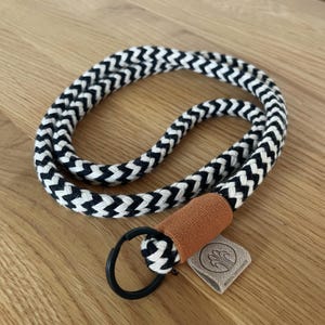 Könnte beinhalten: Schwarz-weißes Lanyard mit Chevron-Muster, braunem Lederpatch und schwarzem Metallschlüsselring. Der Lederpatch trägt den Text "wood & wonder".