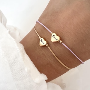 以下が含まれることがあります： 2つの繊細なブレスレット。1つは「Mama」と書かれたハートペンダントが付いたゴールド。もう1つは「Leonie」と書かれたハートペンダントが付いた薄紫色のコード。どちらのハートペンダントもゴールドです。