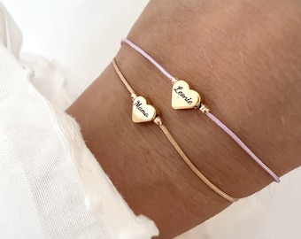 May include: Two delicate bracelets. One is gold with a heart pendant that says "Mama". The other is a light purple cord with a heart pendant that says "Leonie". Both heart pendants are gold.