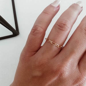 Puede incluir: Un anillo de cadena de oro con un dise&ntilde;o delicado. El anillo se lleva en un dedo con un tono de piel claro.