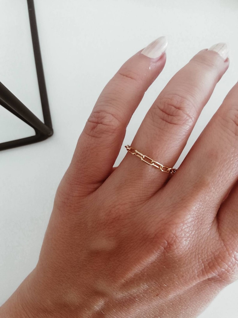 Puede incluir: Un anillo de cadena de oro con un dise&ntilde;o delicado. El anillo se lleva en un dedo con un tono de piel claro.