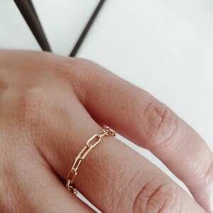 Puede incluir: Un anillo de cadena de oro con un dise&ntilde;o delicado y enlazado. El anillo se lleva en un dedo.