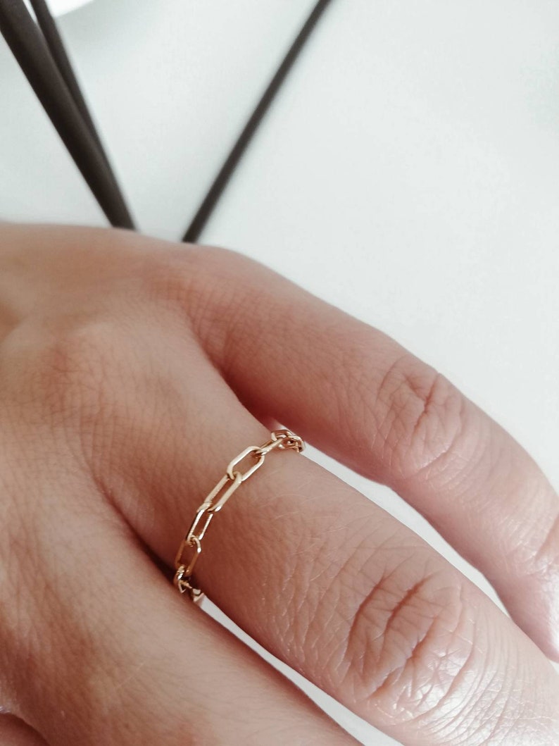 Puede incluir: Un anillo de cadena de oro con un dise&ntilde;o delicado y enlazado. El anillo se lleva en un dedo.