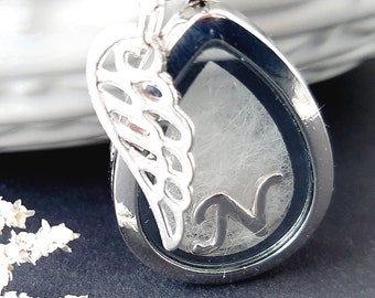 May include: Silver locket necklace with a delicate angel wing charm. The locket is open and contains a small amount of white hair and the letter "N".