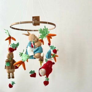 Könnte beinhalten: Ein Holz-Babymobil mit Filztier- und Gemüsedekorationen. Das Mobile zeigt zwei sich umarmende Hasen, Karotten und Erdbeeren. Das Mobile ist an einem Holzring aufgehängt.