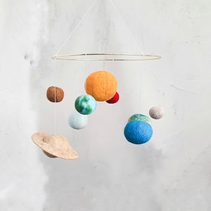 May include: A felt planet mobile with a gold ring, featuring a brown, blue, green, orange, and white planets. The planets are suspended from the ring by white strings.