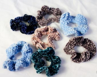 May include: A set of eight scrunchies in various colors, including blue, teal, pink, and brown. The scrunchies are made of a soft, fuzzy material and are perfect for adding a touch of style to any hairstyle.