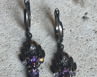 May include: A pair of dangle earrings with a black metal design and purple and clear gemstones.