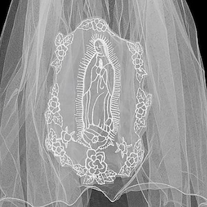 May include: A white veil with a detailed embroidered image of Our Lady of Guadalupe. The veil is made of a sheer, layered fabric, and the text "Our Lady of Guadalupe" is printed on the upper left side.