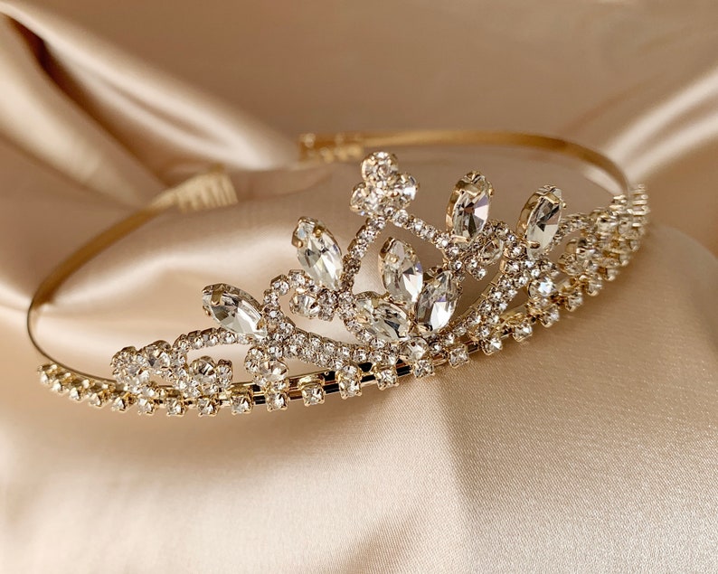 Pode incluir: Uma tiara dourada com strass transparentes e um design delicado. A tiara &eacute; feita de metal e tem um visual cl&aacute;ssico e elegante.