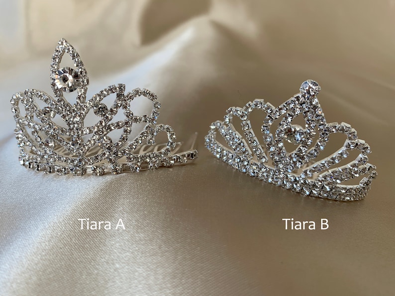 Two mini tiaras are displayed on a gold background. The rounded design is labeled Tiara B, while the slightly elongated design is labeled Tiara A. Both are mini-sized, adorned with rhinestones, and sparkle in the light.