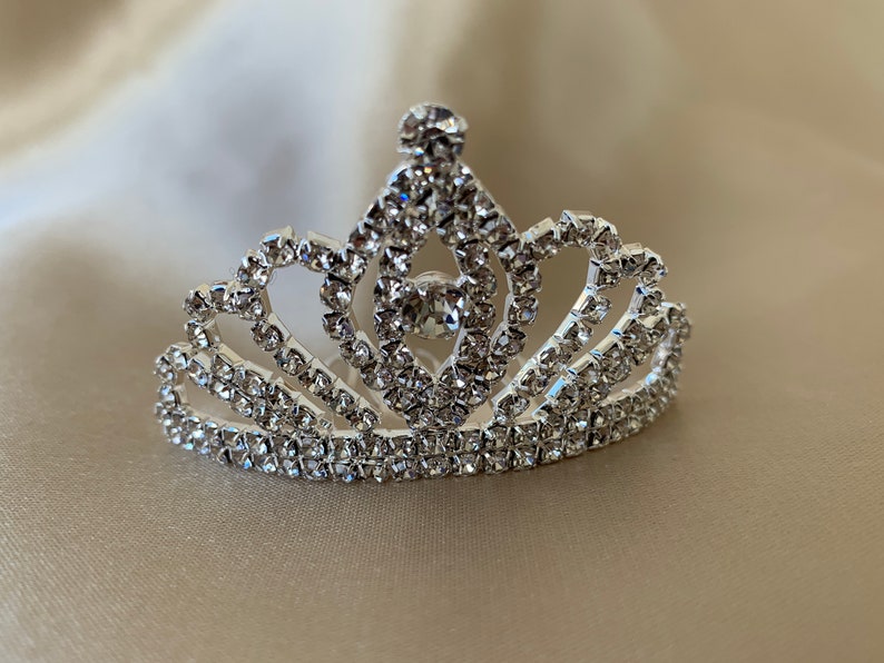 A round-shaped mini tiara set with eye-shaped rhinestones laid sideways is placed on gold fabric.