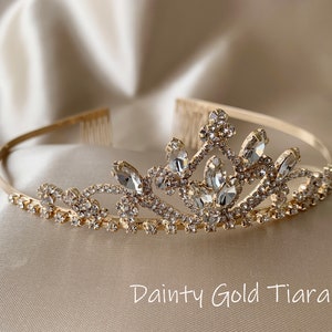 Pode incluir: Uma tiara dourada com detalhes em cristal transparente. A tiara tem um design delicado com um pente na parte de tr&aacute;s para facilitar a coloca&ccedil;&atilde;o no cabelo.