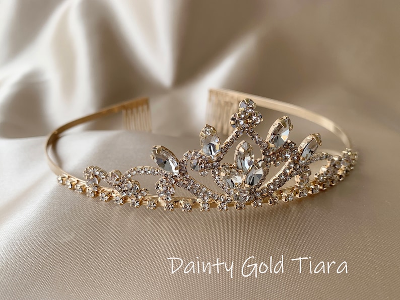 Pode incluir: Uma tiara dourada com detalhes em cristal transparente. A tiara tem um design delicado com um pente na parte de tr&aacute;s para facilitar a coloca&ccedil;&atilde;o no cabelo.