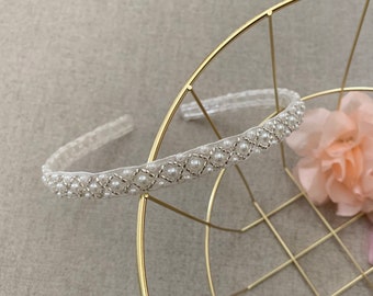 May include: A white headband featuring a delicate pearl and bead design. The headband is made from a thin, flexible material and is ideal for adding a touch of elegance to any outfit.