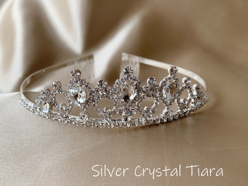 Pode incluir: Uma tiara prateada com detalhes de cristal transparente. A tiara tem um pente na parte de tr&aacute;s para f&aacute;cil fixa&ccedil;&atilde;o no cabelo.