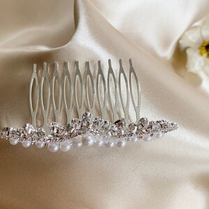May include: A silver hair comb with a row of faux pearls and rhinestones. The comb has a decorative design and is ideal for adding a touch of sparkle to any hairstyle.