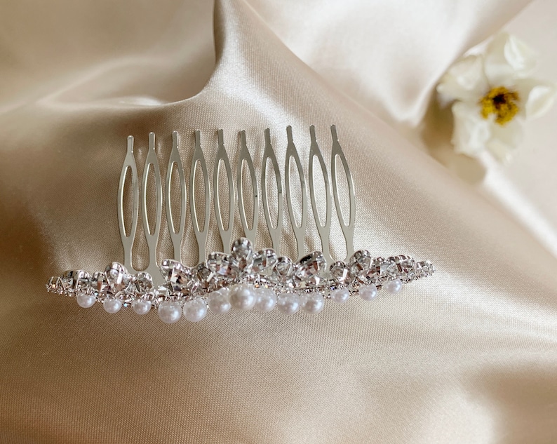 May include: A silver hair comb with a row of faux pearls and rhinestones. The comb has a decorative design and is ideal for adding a touch of sparkle to any hairstyle.