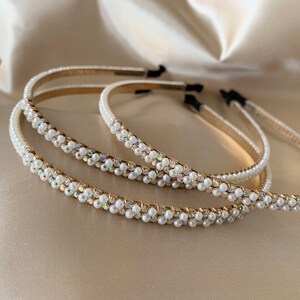 Several pearl-embellished headbands with gold-toned bands are displayed on a satin surface. The headbands feature rows of small, white pearls and iridescent accents, creating a delicate and elegant appearance. The headbands are a hair accessory.