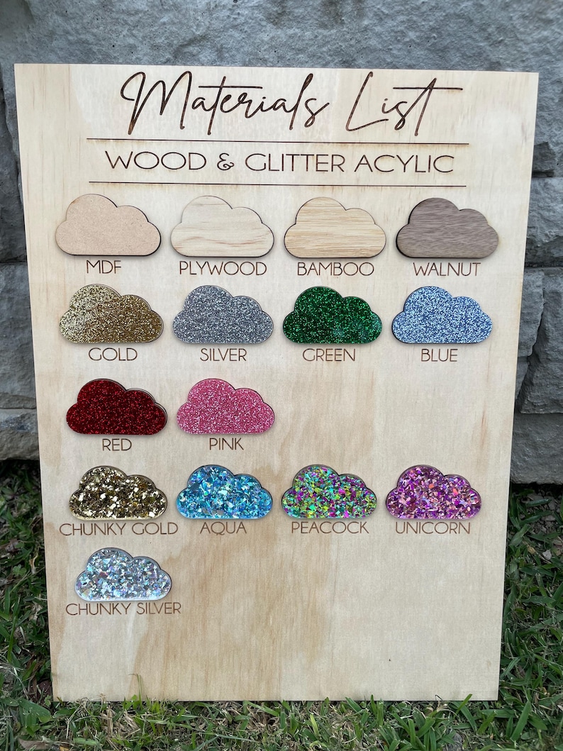 May include: A light wood display board titled Materials List Wood & Glitter Acrylic featuring seventeen cloud-shaped samples labeled MDF, Plywood, Bamboo, Walnut, Gold, Silver, Green, Blue, Red, Pink, Chunky Gold, Aqua, Peacock, Unicorn, and Chunky Silver.