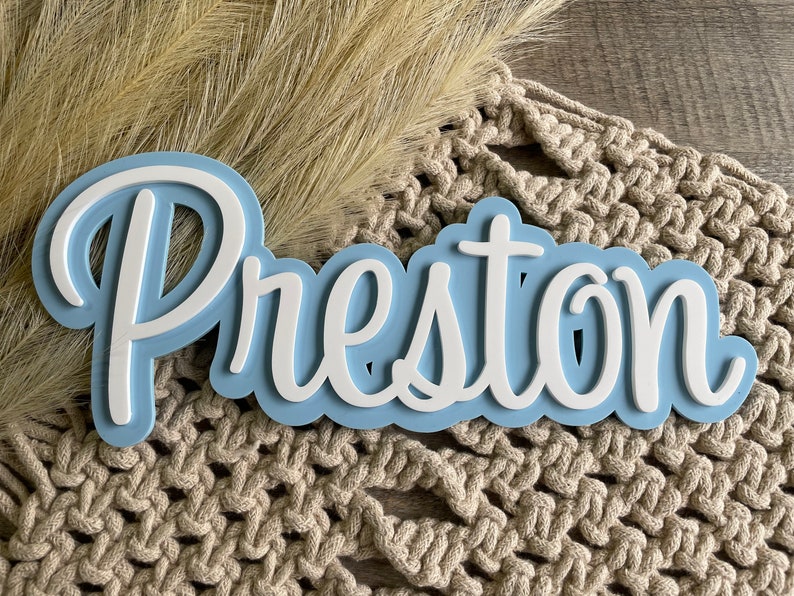 May include: A custom name sign featuring the name Preston in white, raised, cursive lettering layered over a light blue, cloud-shaped backing. The sign has a smooth, matte finish and a layered 3D design that creates depth and visual contrast.