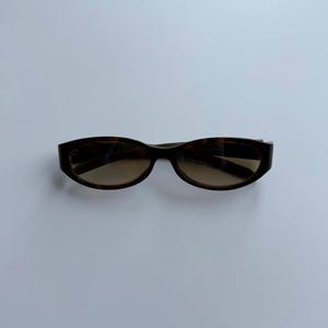 May include: Brown tortoiseshell sunglasses with a rectangular frame and tinted lenses. The sunglasses are a classic accessory, suitable for various styles. The frame has a dark brown pattern, and the lenses are a lighter brown color.