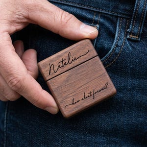 Könnte beinhalten: Eine kleine, rechteckige, dunkelbraune Holzschatulle mit Klappdeckel. Auf dem Deckel steht der Name Natalie in schwarzer Schreibschrift, und auf dem Unterteil ist der Text how about forever? in passender schwarzer Schrift eingraviert.