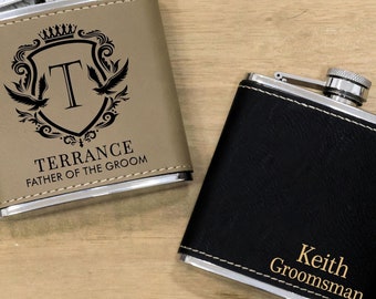 May include: Two personalized stainless steel hip flasks with faux leather coverings. One flask is tan with a black crest and the text "Terrance Father of the Groom". The other flask is black with the text "Keith  Groomsman".