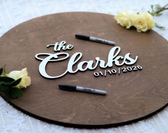 May include: A round wooden sign with the text "The Clarks 01/10/2026" in white lettering. Two black markers are on the sign.