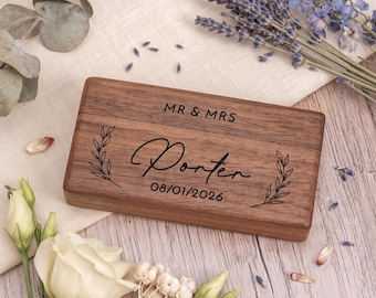 May include: A rectangular dark brown wooden box with a hinged lid. The lid is engraved with the text MR & MRS, the name Porter in a script font, and the date 08/01/2026, flanked by two delicate leaf branch illustrations on the sides.