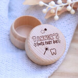 May include: A small wooden box with a lid, engraved with the text "Tanner's Tooth Fairy Box" and a star, a wand, and a tooth graphic. The box is light brown and has a smooth finish.