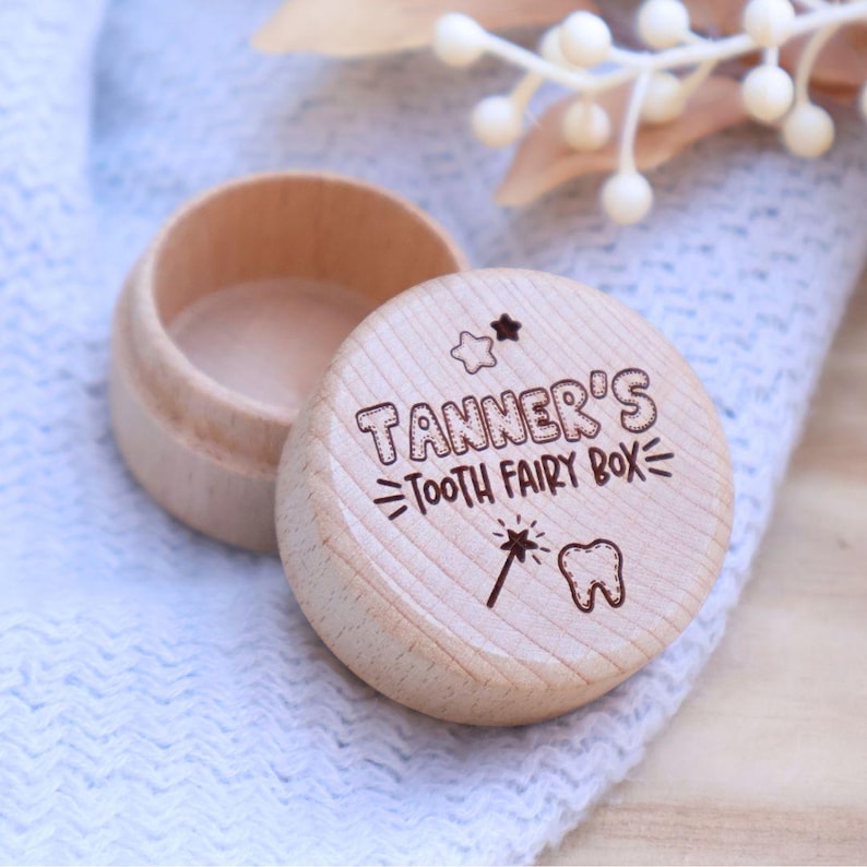 May include: A small wooden box with a lid, engraved with the text "Tanner's Tooth Fairy Box" and a star, a wand, and a tooth graphic. The box is light brown and has a smooth finish.