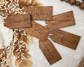 Op de afbeelding: Zes rechthoekige houten cadeaulabels met afgeronde hoeken en een gat aan één uiteinde. Elk label heeft een donkerbruine gebeitste afwerking en is gegraveerd met een unieke naam in zwart cursief schrift: Darnell, Joshua, Stewart, Colby, Tiffany en Angelina.
