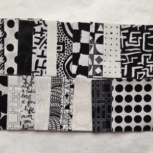 Può includere: Una collezione di campioni di tessuto in bianco e nero con vari motivi, tra cui pois, forme geometriche e disegni astratti. Alcuni campioni hanno testo. I tessuti sono disposti in forma rettangolare.