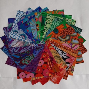 Könnte beinhalten: Eine kreisförmige Anordnung farbenfroher Stoffquadrate. Die Quadrate zeigen eine Vielzahl von Mustern, darunter florale, geometrische und abstrakte Designs in Blau-, Grün-, Orange-, Rot- und Lilatönen. Der Stoff scheint Baumwolle oder ein ähnliches Material zu sein.