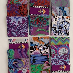 May include: A collection of small, rectangular fabric swatches with various floral and abstract patterns. The swatches feature a range of colors, including purple, blue, orange, and green. The fabrics appear to be cotton or a similar material.