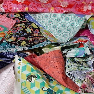 Könnte beinhalten: Eine Sammlung bunter Stoffreste mit verschiedenen Mustern. Die Stoffe weisen Blumen-, geometrische und Tiermuster in Rosa, Grün, Blau und Gelb auf. Einige Stoffe haben Goldfisch-, Meerschweinchen- und Blattdesigns.
