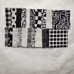 Pode incluir: Uma cole&ccedil;&atilde;o de amostras de tecido em preto e branco com v&aacute;rios padr&otilde;es, incluindo bolinhas, formas geom&eacute;tricas e desenhos abstratos. As amostras est&atilde;o dispostas em duas fileiras sobre uma superf&iacute;cie branca, mostrando uma variedade de texturas e estilos.
