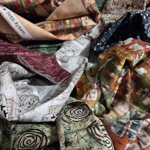 May include: A collection of patterned fabric scraps in various colors and designs. The fabrics include map-like prints, abstract patterns, and text that reads "Seth Apter." Colors include beige, burgundy, green, and blue. The fabrics are crumpled and layered.