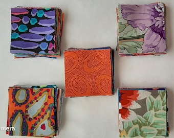 May include: Stacks of colorful fabric squares in various patterns. The fabrics feature designs in shades of purple, teal, orange, and floral prints. The squares are arranged on a white surface, showcasing the variety of textiles.