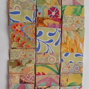May include: A collection of small, folded fabric squares with various floral and abstract patterns. The fabrics feature a mix of colors, including yellow, orange, pink, and blue. The arrangement suggests a craft or textile project.