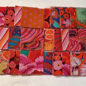 May include: A collection of colorful fabric squares in various patterns and designs. The squares feature vibrant hues of red, orange, pink, blue, and green, with floral, polka dot, and abstract motifs. The fabric appears to be cotton or a similar material.