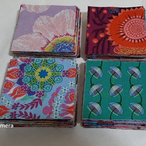Könnte beinhalten: Vier Stapel bunter Stoffquadrate mit floralen und geometrischen Mustern. Die Quadrate weisen Designs in Lila, Rosa, Orange, Türkis und Blau auf. Der Stoff scheint Baumwolle oder ein ähnliches Material zu sein, das sich für Quilt- oder Bastelprojekte eignet.