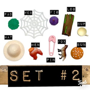 May include: A collection of miniature items labelled PAD, WEB, FIG, LOG, CUP, HAT, HEN, PIN, FOX, and BUN, arranged above a wooden ruler showing SET #2. The items include a green pad, white web, purple fig, brown log, cup, hat, hen, pink pin, fox, and bun.
