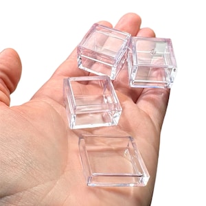 May include: Four clear plastic square boxes with lids. The boxes are small and are stacked on top of each other.