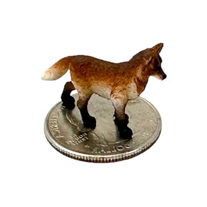 May include: A small, brown and white fox figurine standing on a US quarter. The figurine is about the size of a quarter.