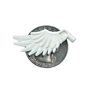 May include: White plastic angel wings with a textured surface. The wings are about the size of a US quarter.