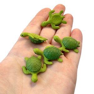 May include: Five small, green turtle figurines with detailed shell patterns. The turtles are in various poses, with their flippers and heads visible. The figurines are a light green color and appear to be made of plastic or a similar material.