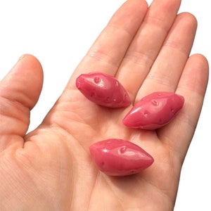 May include: Three pink sweet potato shaped candies in a hand.
