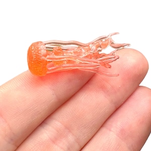 May include: A small, translucent, orange-colored jellyfish figurine. The figurine is made of resin and has a detailed, realistic design.